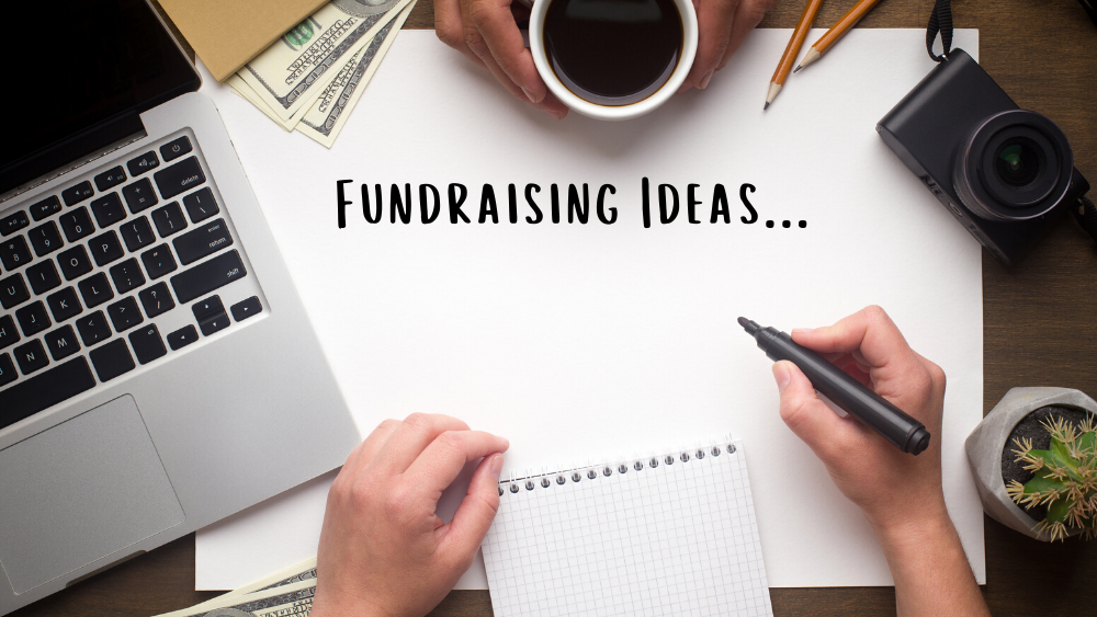 Two people sitting across from each other with a computer, pad of paper, and a paper with the words "Fundraising Ideas..." 