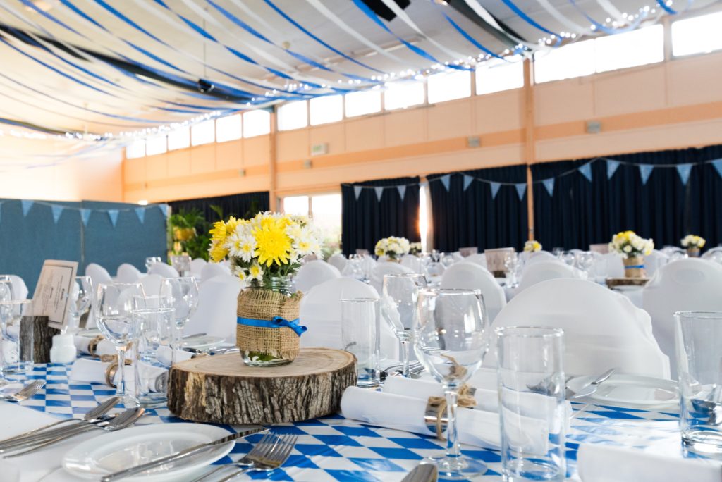 Banquet hall full of tables set for an event. Bouquet of daisies sit in a vase on top of a wooden center piece