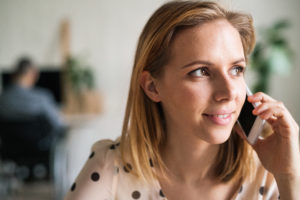 Smiling woman talking on the phone while a person stands out of focus behind her