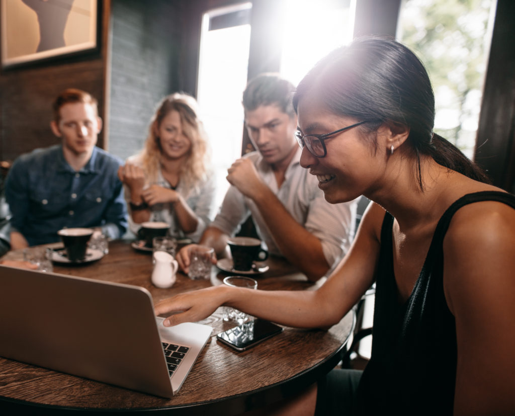 Group of laughing people gathered around a laptop